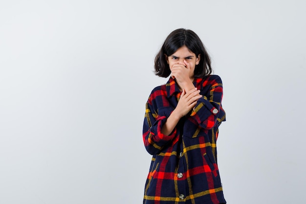 Young girl covering mouth with hand in checked shirt and looking exhausted. front view.
