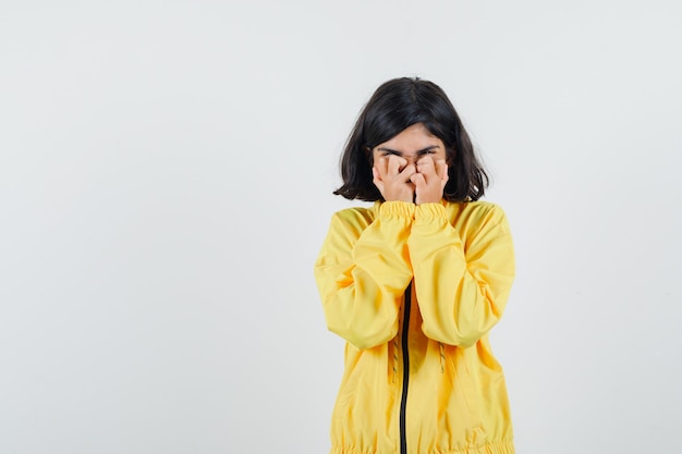Young girl covering part of face with hands in yellow bomber jacket and looking dismal