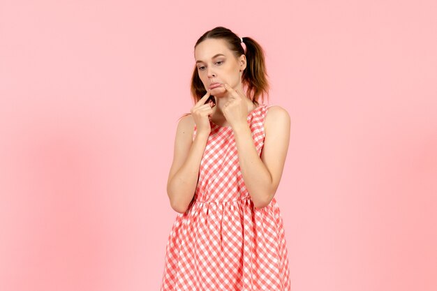 young girl in cute bright dress with sad expression on pink