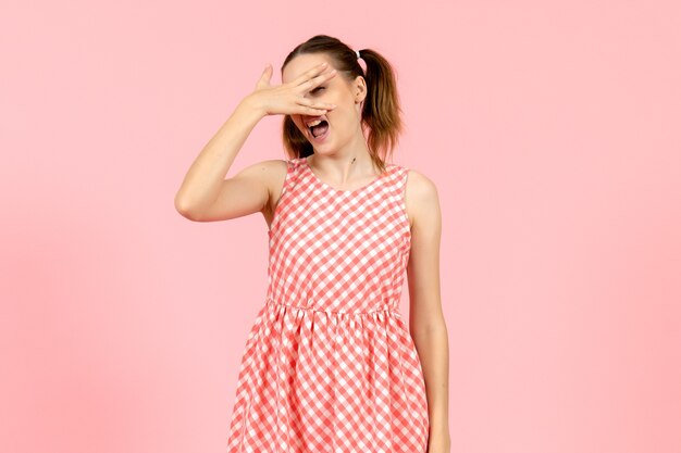 young girl in cute pink dress covering her face on pink