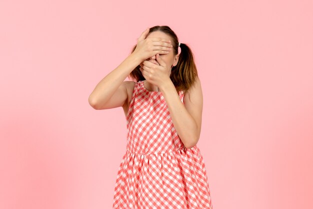 young girl in cute pink dress covering her face on pink