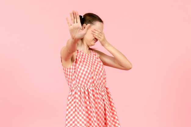 Giovane ragazza in abito rosa carino che copre il viso in rosa