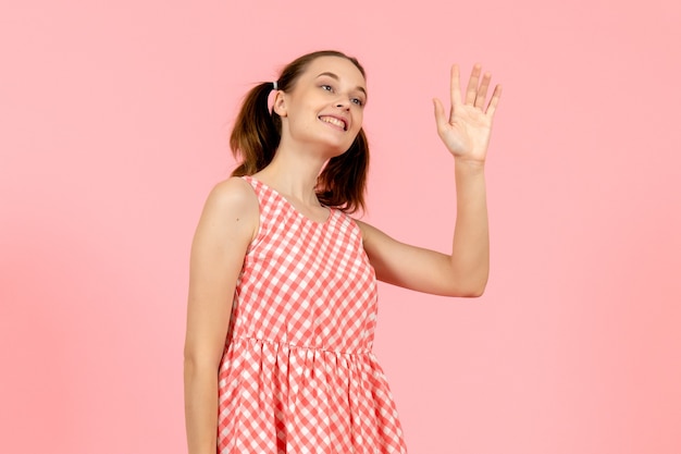 young girl in cute pink dress greeting someone with smile on pink