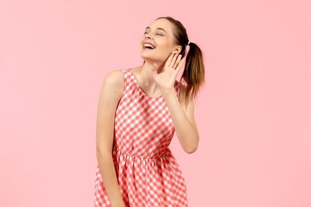young girl in cute pink dress listening closely and smiling on pink