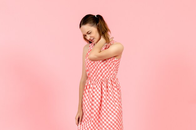 young girl in cute pink dress suffering from neck pain on pink