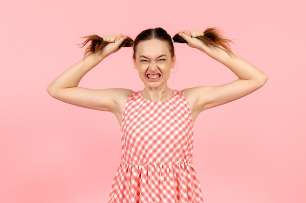 Free photo young girl in cute pink dress with angry expression on pink