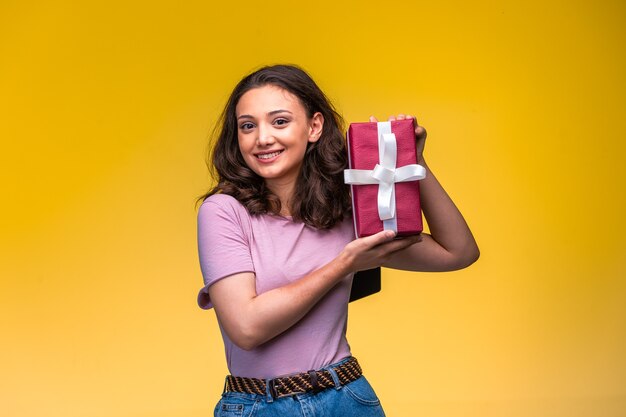 Young girl demonstrating her gift box on yellow wall.
