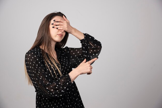 Young girl in dress covering eyes by hands and pointing aside up.