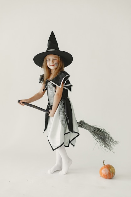 魔女に扮した黒い服を着た少女は、頭に円錐形の帽子をかぶっています。ほうきに座ってカボチャを持っている女の子