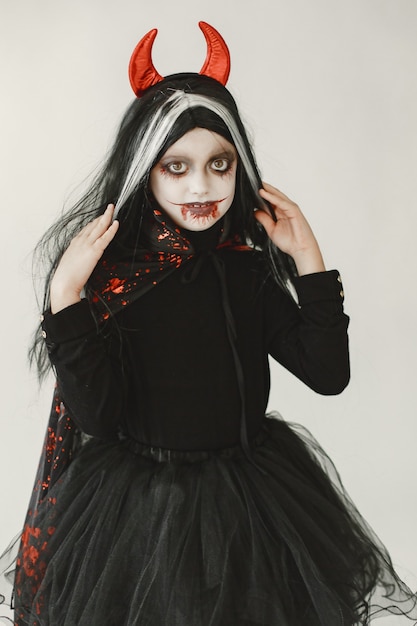 Free photo young girl dressed in black dress as a devil has a two red horns on her head