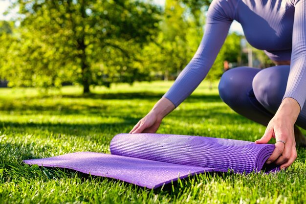 Young girl dressed in yoga clothes holding her ecofriendly yoga mat on the green grass in the park