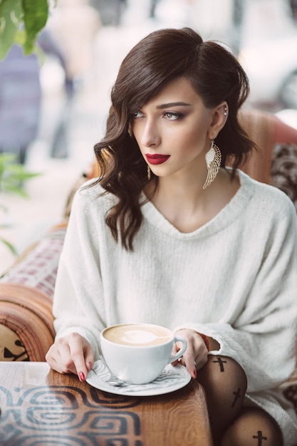 Молодая девушка пьет кофе в модном кафе