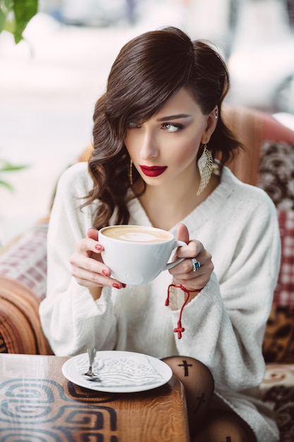 Молодая девушка пьет кофе в модном кафе