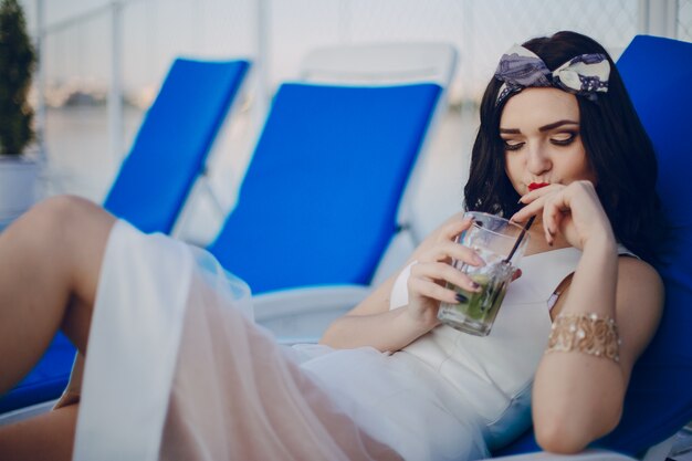 Young girl drinking a drink while lying on a blue hammock