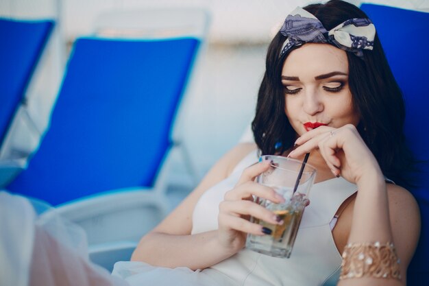 Young girl drinking a drink while lying on a blue hammock