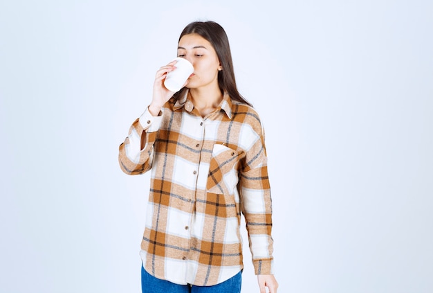 白い壁にお茶のプラスチックカップを飲む少女。