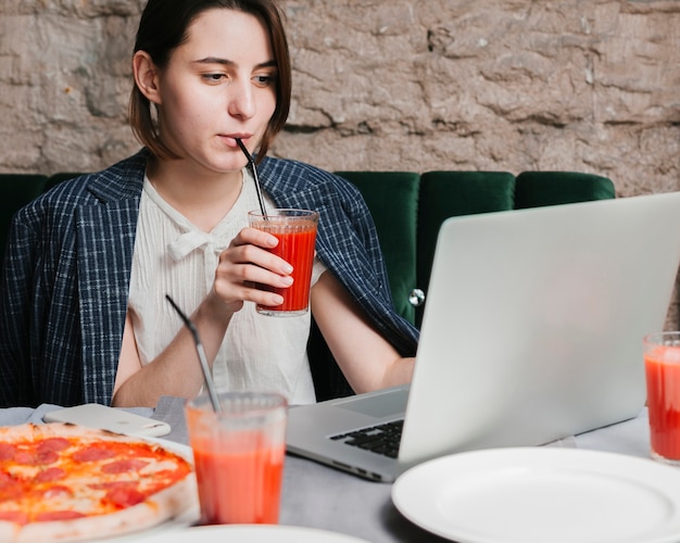 Ragazza che beve il frullato e che lavora al computer portatile