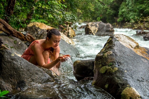 Free photo a young girl drinks water from a mountain stream