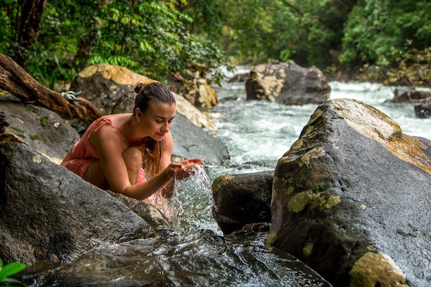 A young girl drinks water from a mountain stream