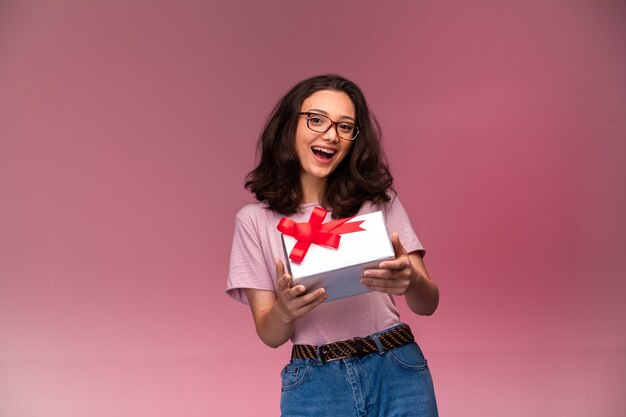 Young girl in eyeglasses offering a white gift box and smiling. 