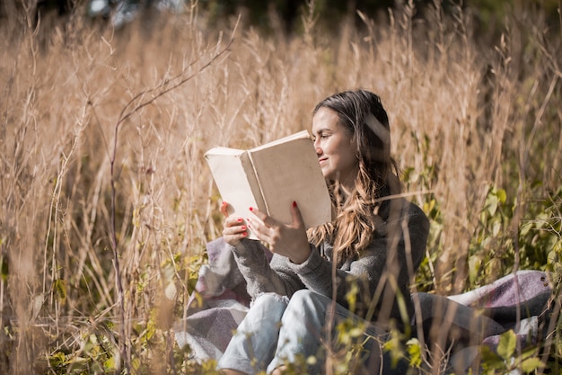 молодая девушка на поле читает книгу