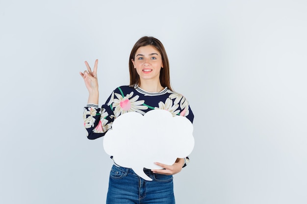 Free photo young girl in floral blouse, jeans showing v-sign and looking happy , front view.