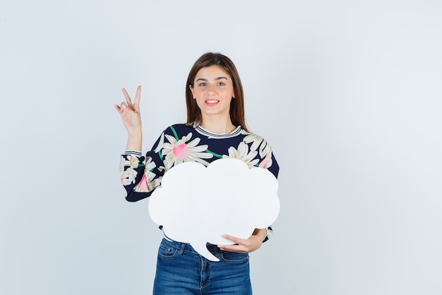 Young girl in floral blouse, jeans showing V-sign and looking happy , front view.