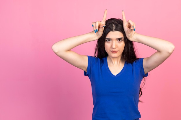 Young girl gesture horn with her fingers and stand on pink background