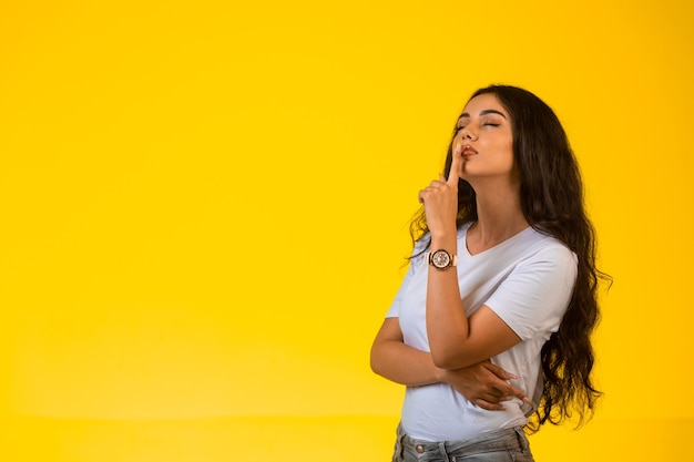 Young girl gives silence sign in a romantic way on yellow surface