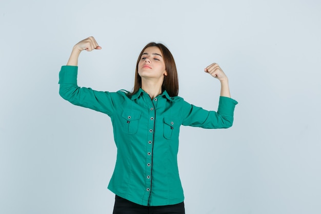 Young girl in green blouse, black pants showing winner gesture and looking lucky , front view.