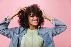 Free photo young girl in green t-shirt smiles and dances on pink wall. cool woman touches her curly hair