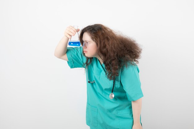 Giovane ragazza in uniforme verde che tiene un barattolo di vetro con liquido blu.