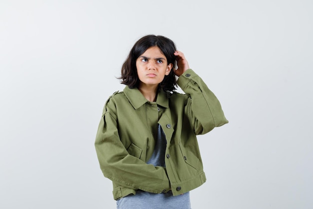 Free photo young girl in grey sweater, khaki jacket, jean pant scratching head, looking away and looking pensive , front view.
