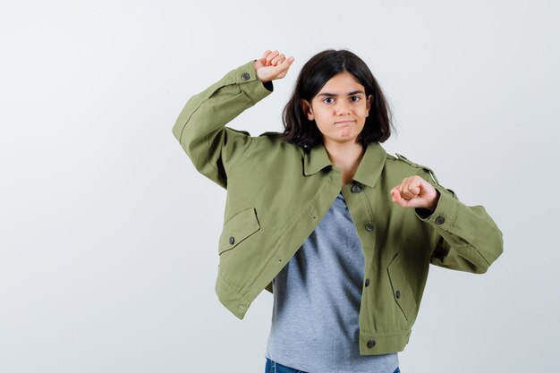 Young girl in grey sweater, khaki jacket, jean pant showing winner pose and looking happy , front view.