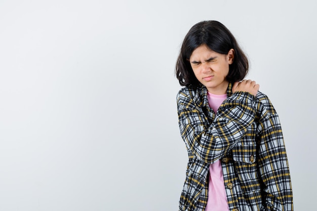 Free photo young girl having shoulder pain in checked shirt and pink t-shirt and looking exhausted. front view.