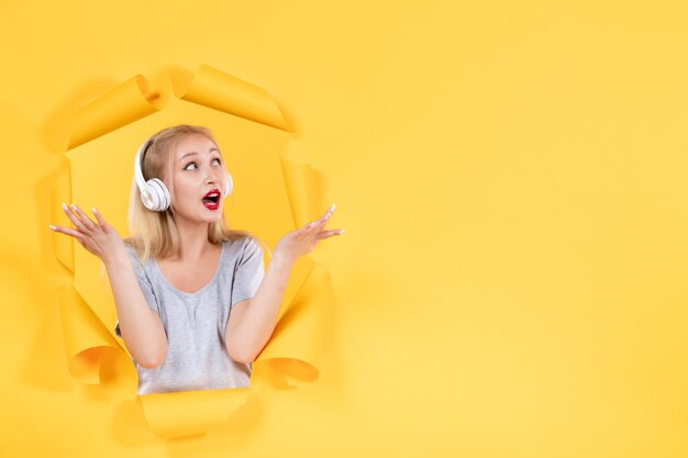 Young girl in headphones on torn yellow paper surface