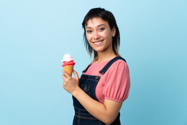 Молодая девушка держит мороженое корнет над синей стеной, много улыбаясь