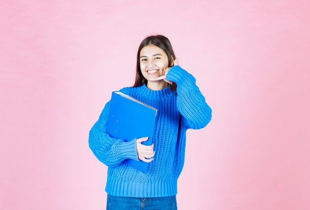 young girl holding a blue folder and showing call sign on pink.