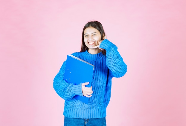 young girl holding a blue folder and showing call sign on pink.