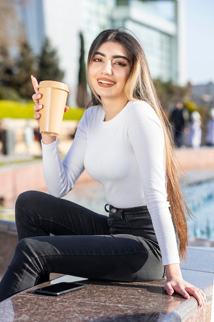 一杯のコーヒーを持って公園に座っている若い女の子高品質の写真