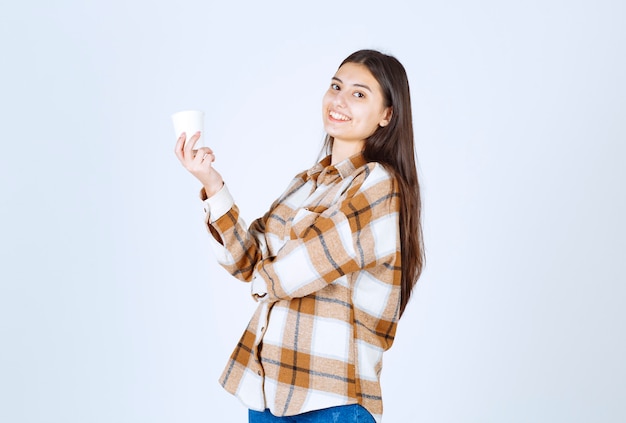 young girl holding cup of tea on white wall. 