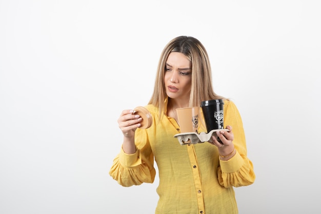 young girl holding cups of coffee and looking at lid.