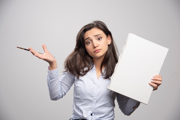 Young girl holding empty canvas and paintbrush with unreadable expression. 