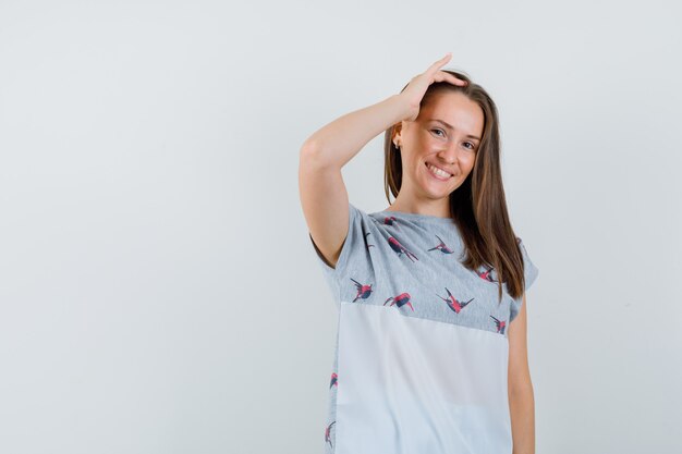 Young girl holding fingers in hair in t-shirt and looking cheerful , front view.