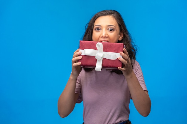 Young girl holding a gift box to her mouth.