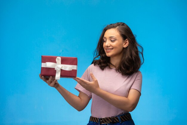 Young girl holding a gift box and smiling while looking to it. 