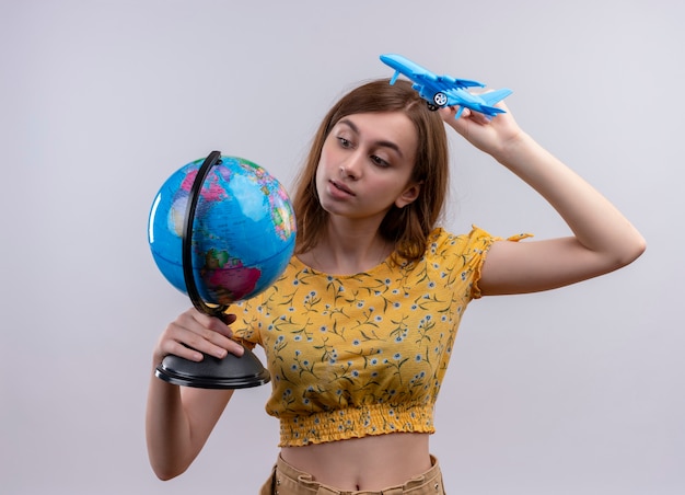 Ragazza che tiene globo e aereo modello e guardando il globo sul muro bianco isolato