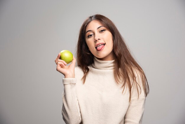 A young girl holding a green apple on a gray wall.