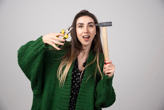 A young girl holding a hammer and pliers in her hands.