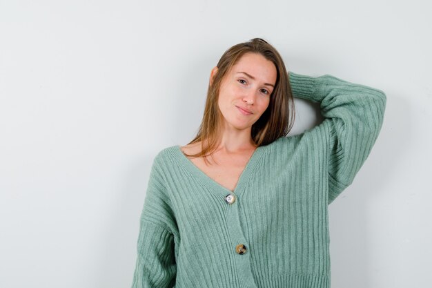 Young girl holding hand behind head in knitwear and looking attractive , front view.